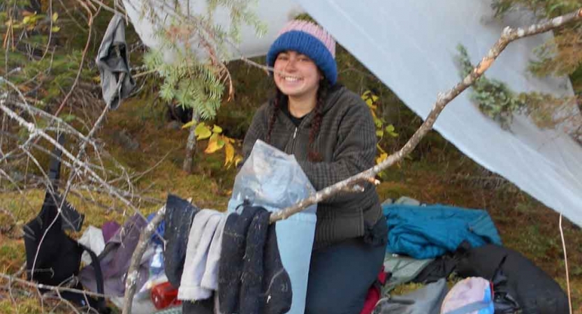 a student hangs clothes on a branch beside a tarp shelter on an outward bound course